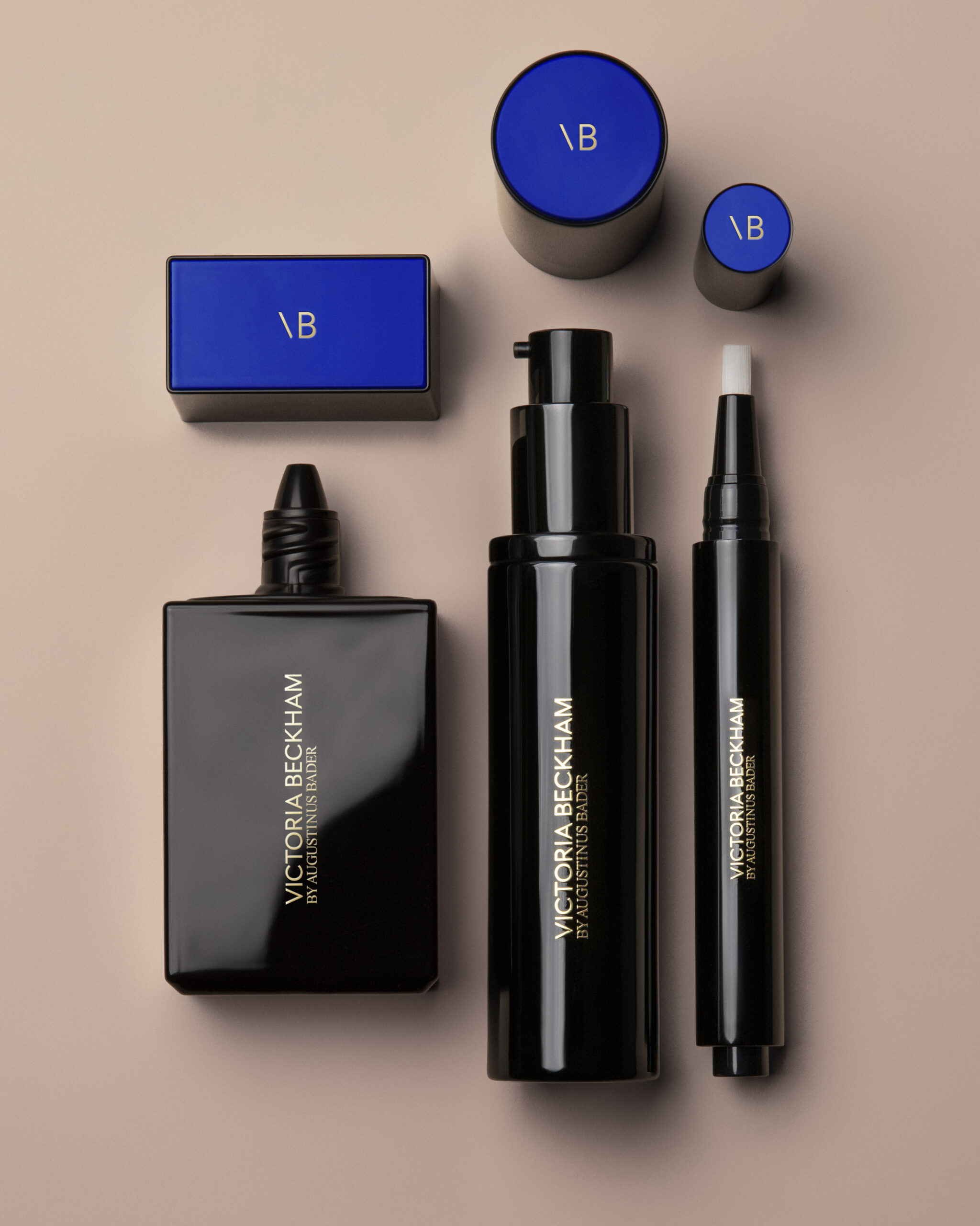 Flat lay of luxury skincare bottles and blue-lidded boxes on a beige background, branded Victoria Beckham by Augustinus Bader (VB).