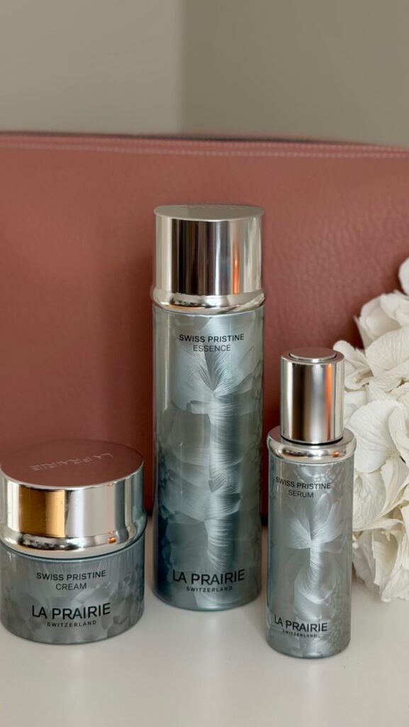 La Prairie Swiss Pristine skincare lineup with cream jar, essence, and serum on a white surface.