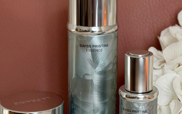 La Prairie Swiss Pristine skincare lineup with cream jar, essence, and serum on a white surface.