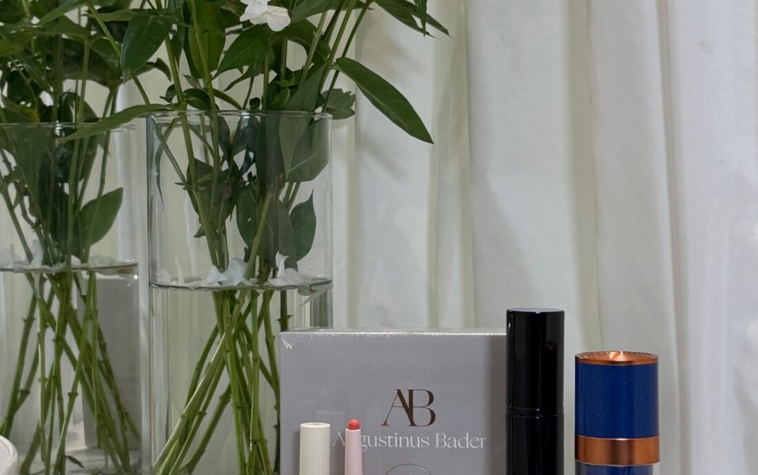 White flower arrangement in glass vases behind a cosmetics display on a countertop with lipsticks and palettes nearby.